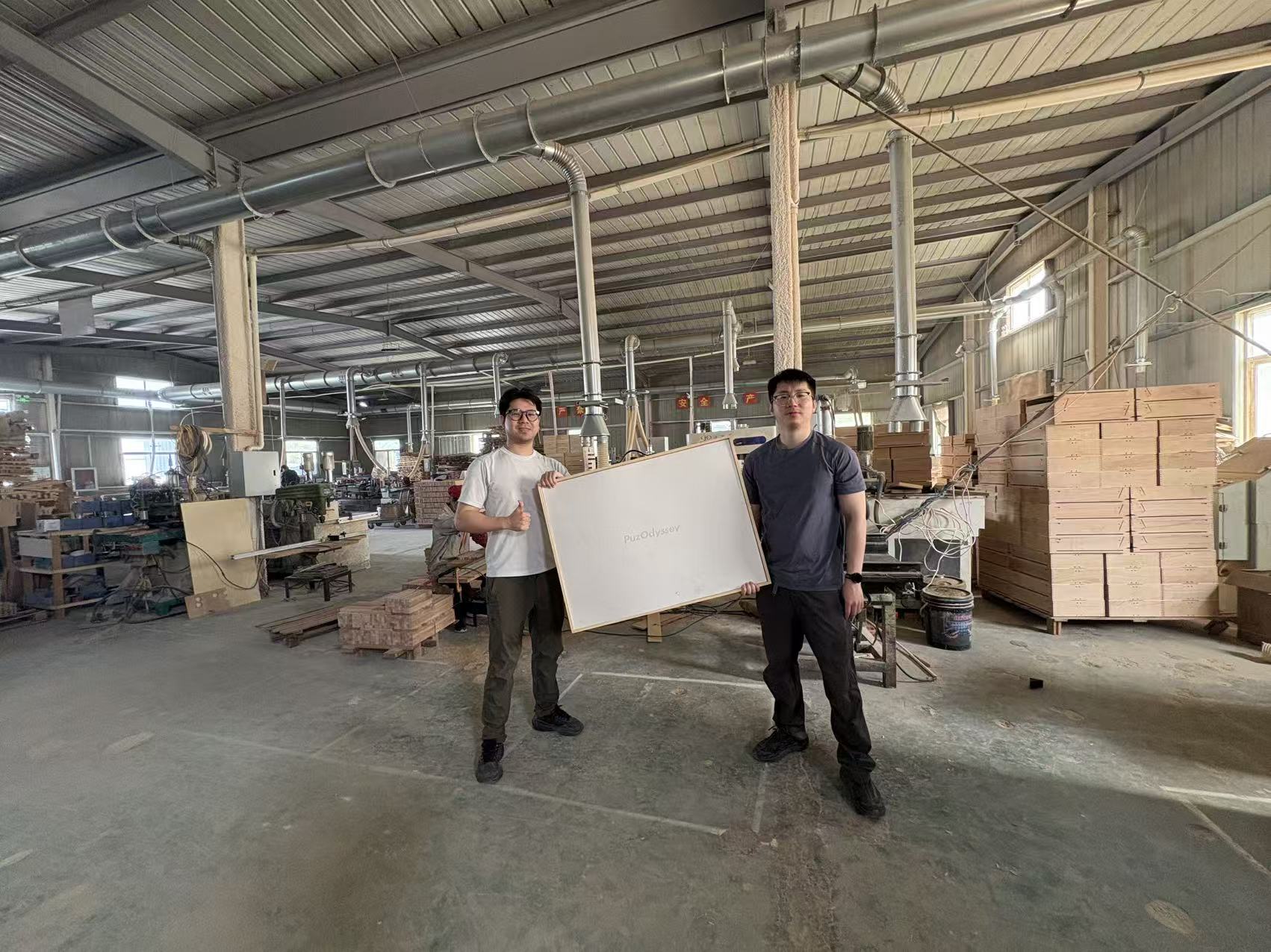 PuzOdyssey's two founders holding a puzzle board at the factory